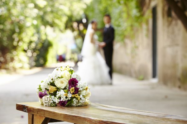 bouquet on wooden bench with bride and groom in the background, focus on the flowers.
